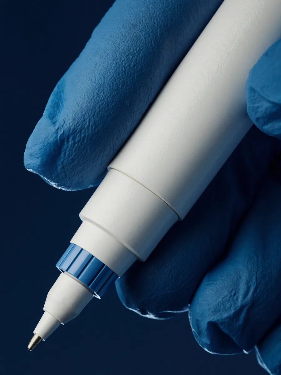 Close-up of a gloved hand holding a white injector pen.